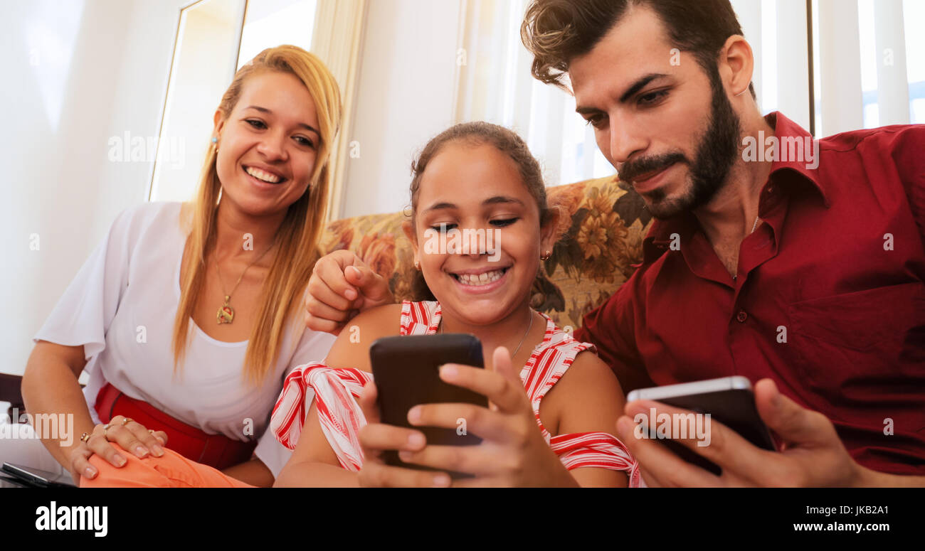 Glückliche Familie zu Hause. Mutter, Vater und Kind mit dem Handy. Mann, Frau und junges Mädchen spielen Spiel auf Mobiltelefonen Stockfoto