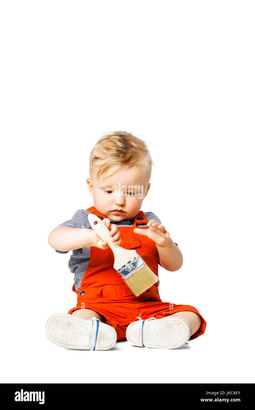 Baby Junge auf dem Boden sitzend hält Pinsel, isoliert auf weiss Stockfoto