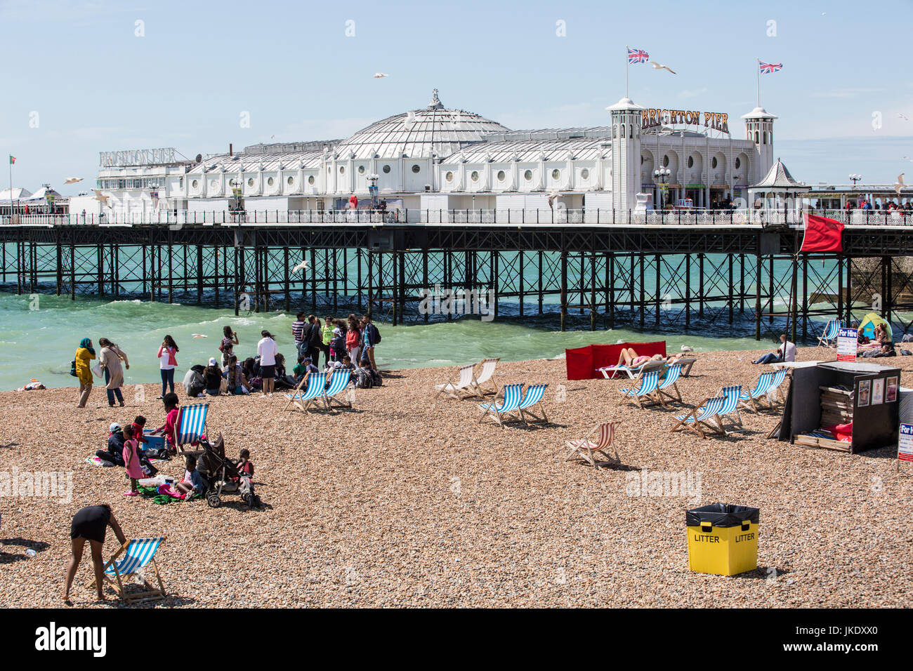 Menschen am Strand neben Brighton Pier an der Südküste von England, an einem sonnigen Tag. Stockfoto