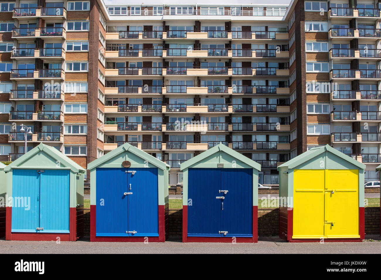 Strandhütten im Vordergrund, mit modernen Wohnhaus hinter, in Brighton an der Südküste von England. Stockfoto