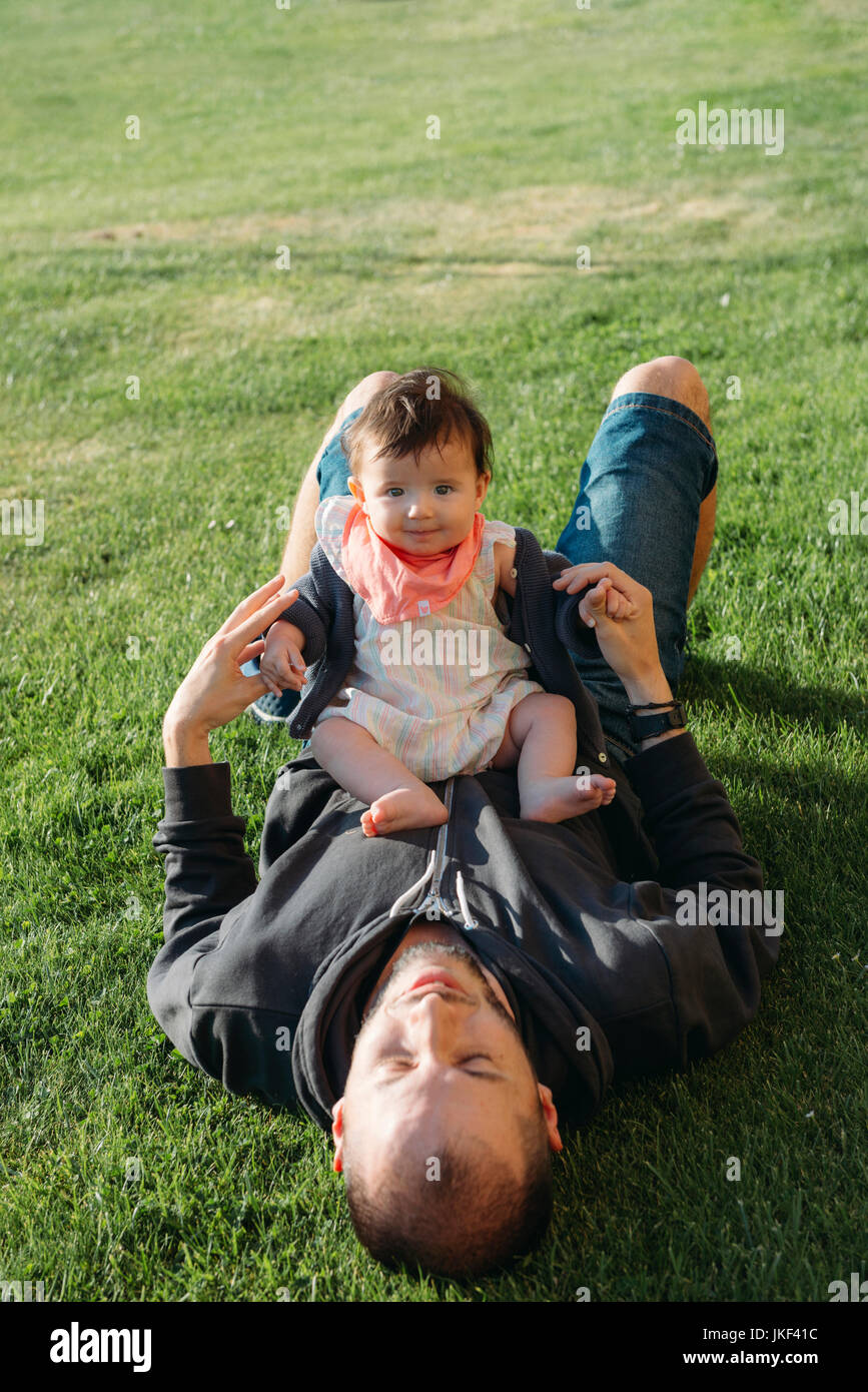 Cute Baby Mädchen sitzen auf ihres Vaters Bauch in einer Wiese Stockfoto
