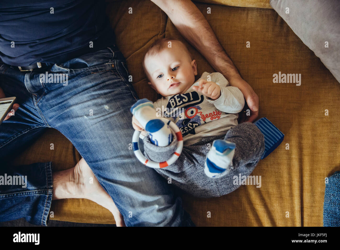 Baby Boy liegen auf der Couch neben seinem Vater mit Smartphone Stockfoto