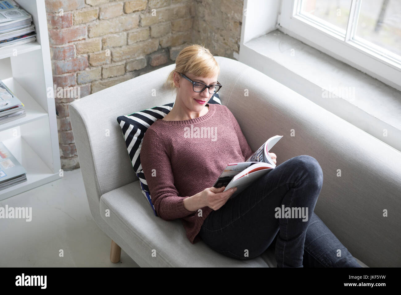 Frau sitzt auf der Couch, Buch lesen Stockfoto