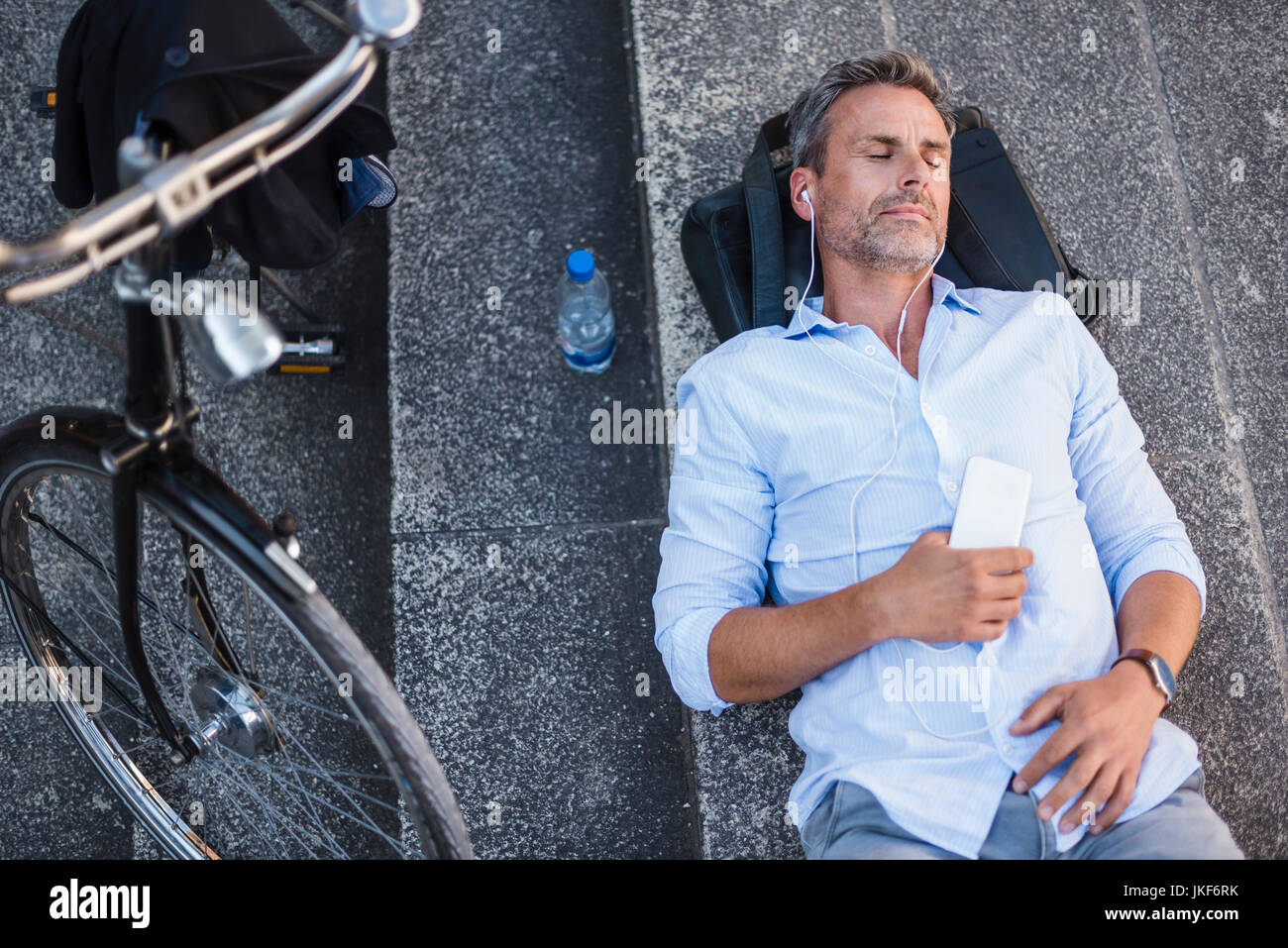 Mann mit geschlossenen Augen liegen auf Treppen mit Handy und Ohrhörer Neben fahrrad Stockfoto
