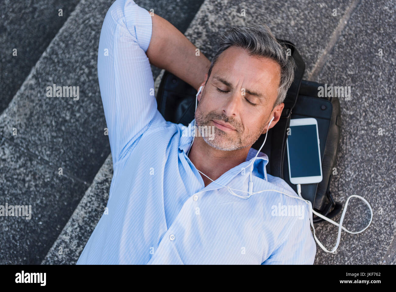Mann mit geschlossenen Augen liegen auf Treppen mit Handy und Ohrhörer Stockfoto