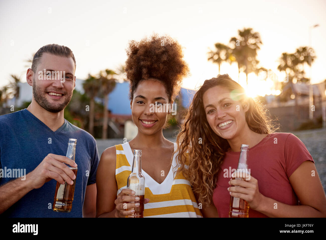 Gruppenbild der drei Freunde mit Bierflaschen am Strand bei Sonnenuntergang Stockfoto