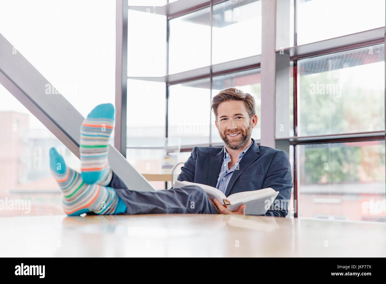 Portrait von lächelnden Geschäftsmann seine Füße auf den Tisch lesen Buch setzen Stockfoto
