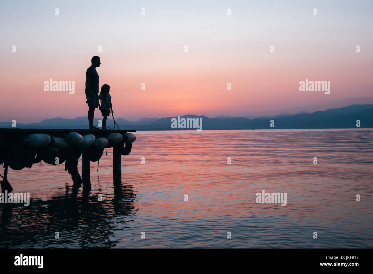 Italien, Lazise, Vater und Tochter stehen auf Jetty suchen am Gardasee bei Sonnenuntergang Stockfoto