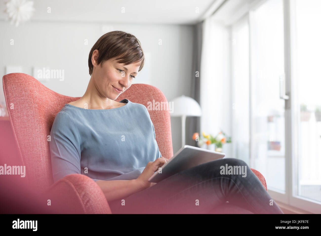 Portrait von Frau sitzt auf einem Sessel mit Tablet home Stockfoto