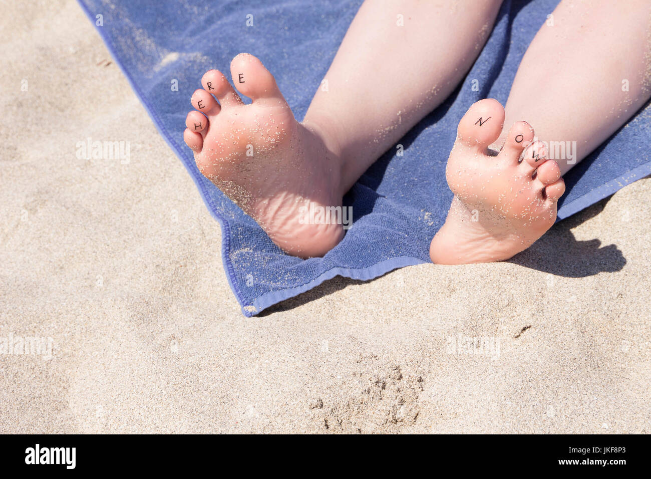 Die Füße der Frau mit Schreiben "Hier und Jetzt" an den Zehen Stockfoto