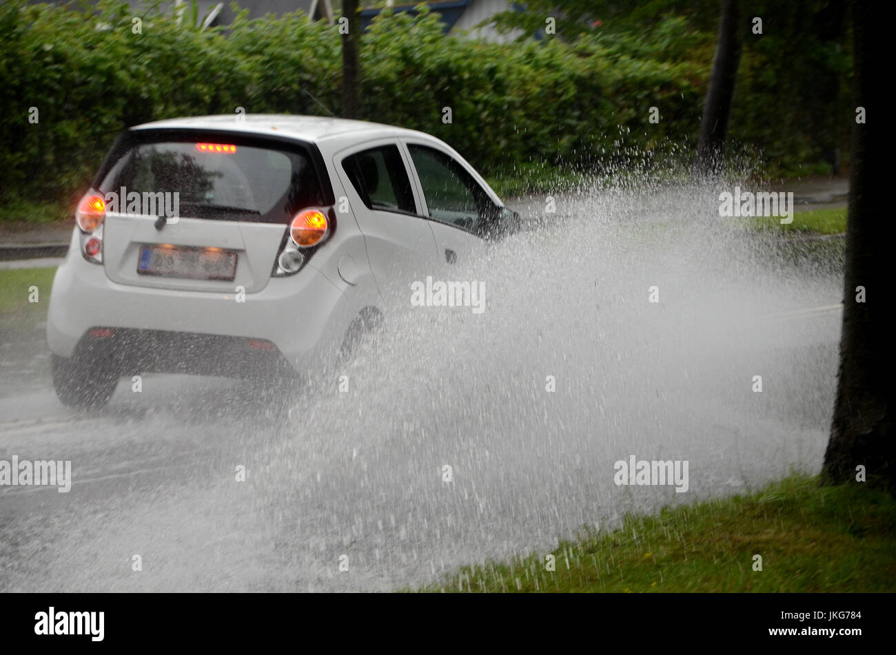 Auto spritzt Tränkewasser auf eine teilweise überfluteten Straße. Stockfoto