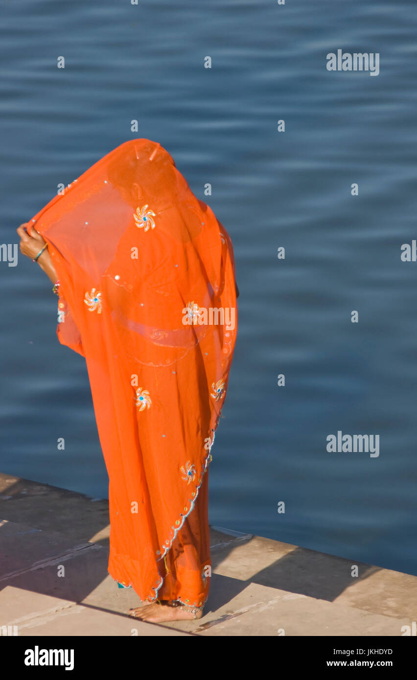 Indische Dame in orange Sari auf Stufen an einem See stehend. Pushkar Rajasthan Indien Stockfoto