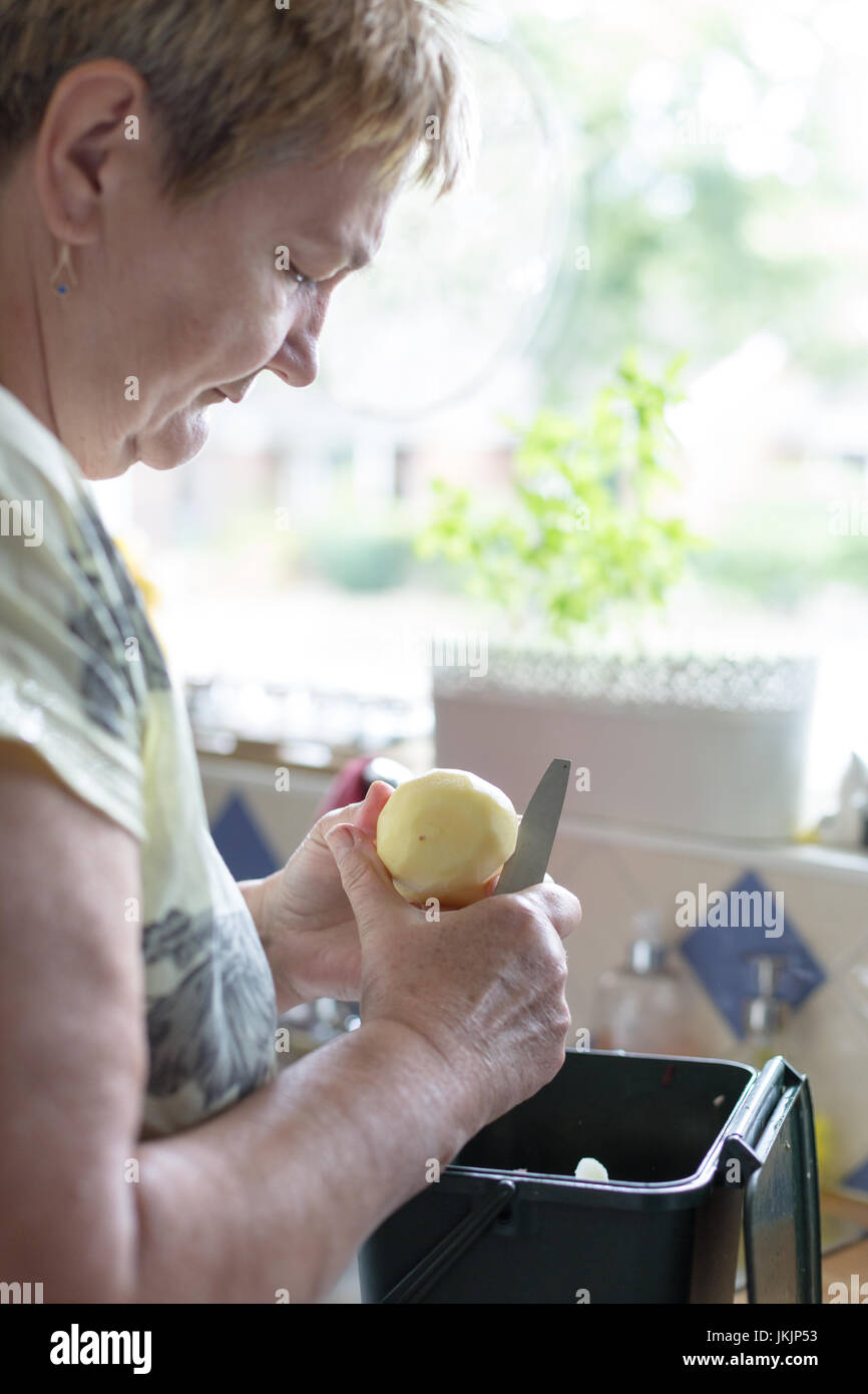 Ältere Frau schneidet geschälte Kartoffel, Zubereitung von Speisen. Vertikale Ausrichtung mit selektiven Fokus auf Kartoffel und Messer. Tageslicht Stockfoto