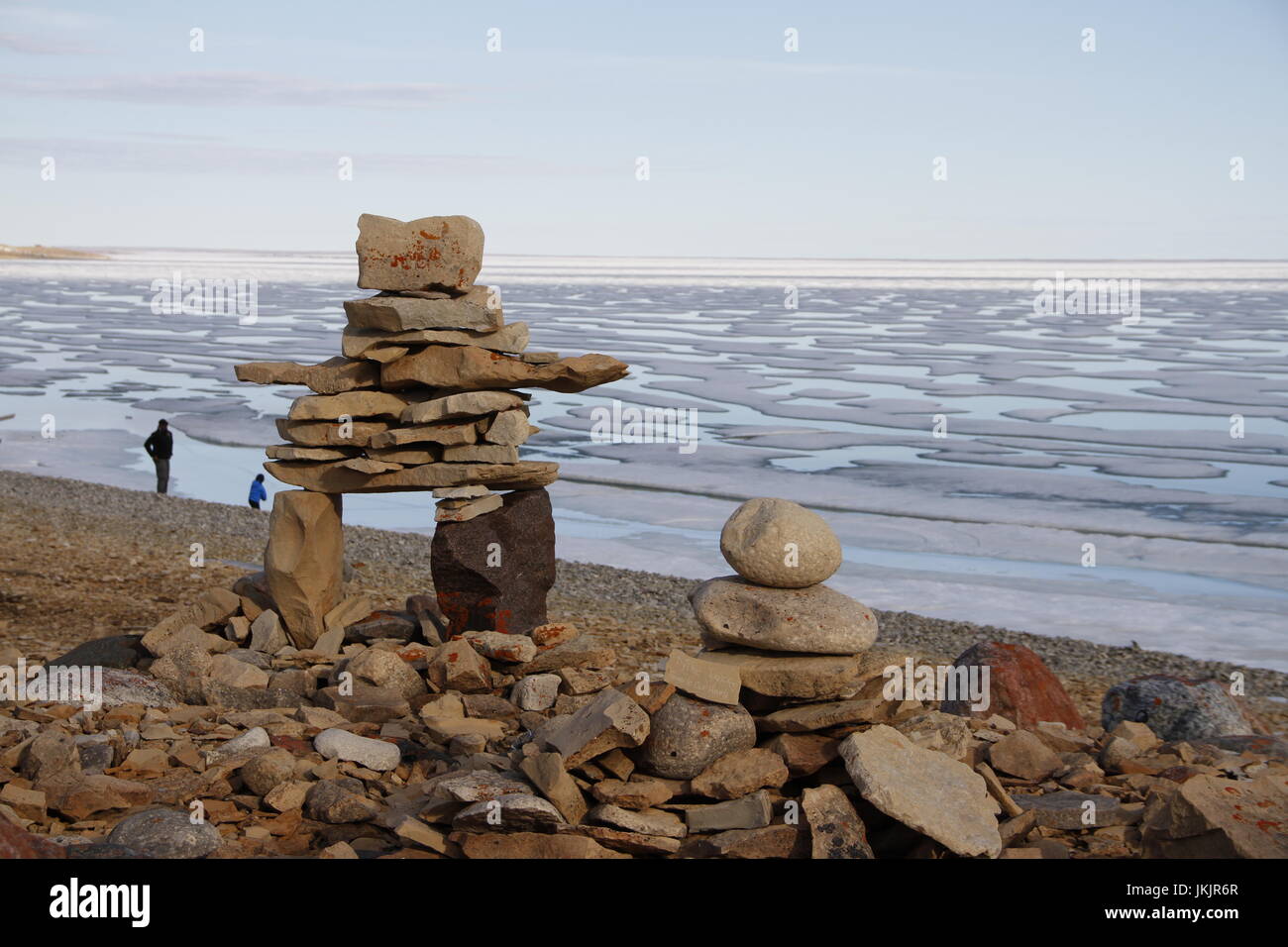 Inukshuk oder Inuksuk auf einem felsigen Strand mit Eis auf dem Ozean Ende Juni in der hohen Arktis in der Nähe der Gemeinde von Cambridge Bay Stockfoto