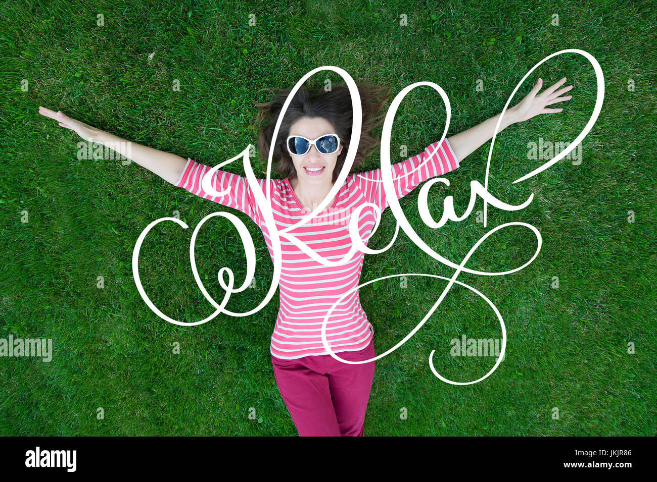 Schöne junge Frau im Freien. Genießen Sie die Natur. Gesundes Lächeln Mädchen in Green Grass und Kalligraphie Schrift Wort Relax Stockfoto