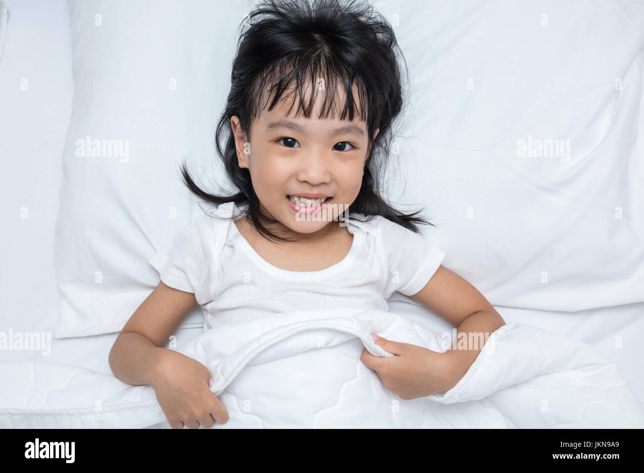 Asiatische chinesische Mädchen liegend auf dem Bett isoliert auf weißem Hintergrund Stockfoto