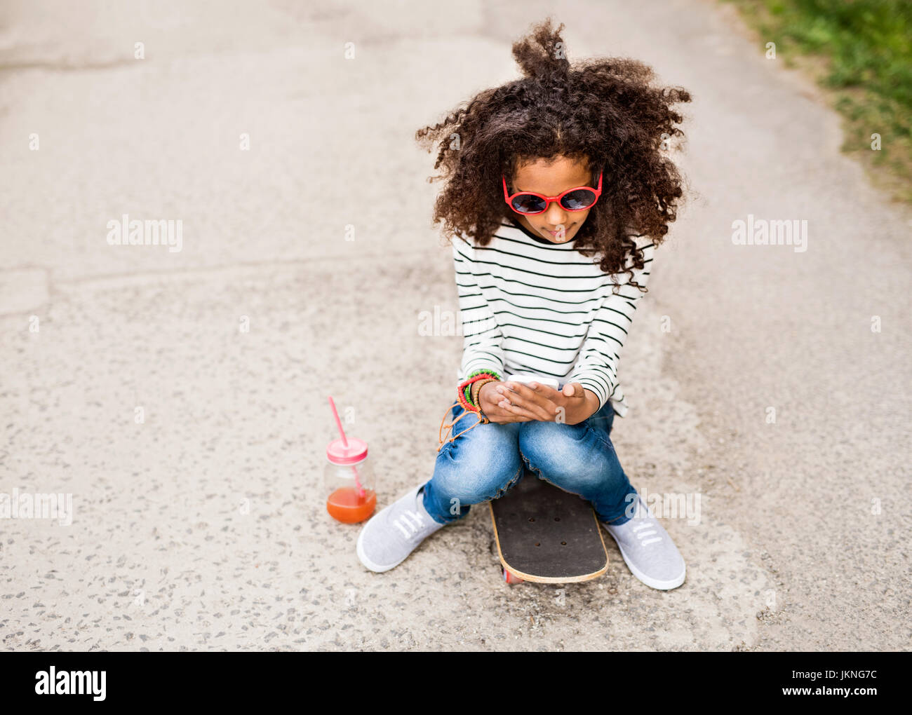 Schöne afrikanische amerikanische Mädchen mit Smartphone und Skateboard. Stockfoto