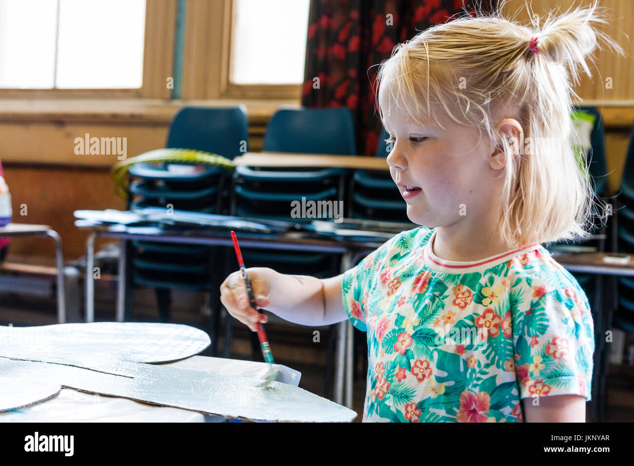 Kaukasische blonde Kind, Mädchen, 5-6 Jahre alt, Malen mit der kleinen Bürste. Kopf und Schultern. Seite anzeigen.. Drinnen in Kunst und pädagogische Werkstatt Handwerk. Stockfoto