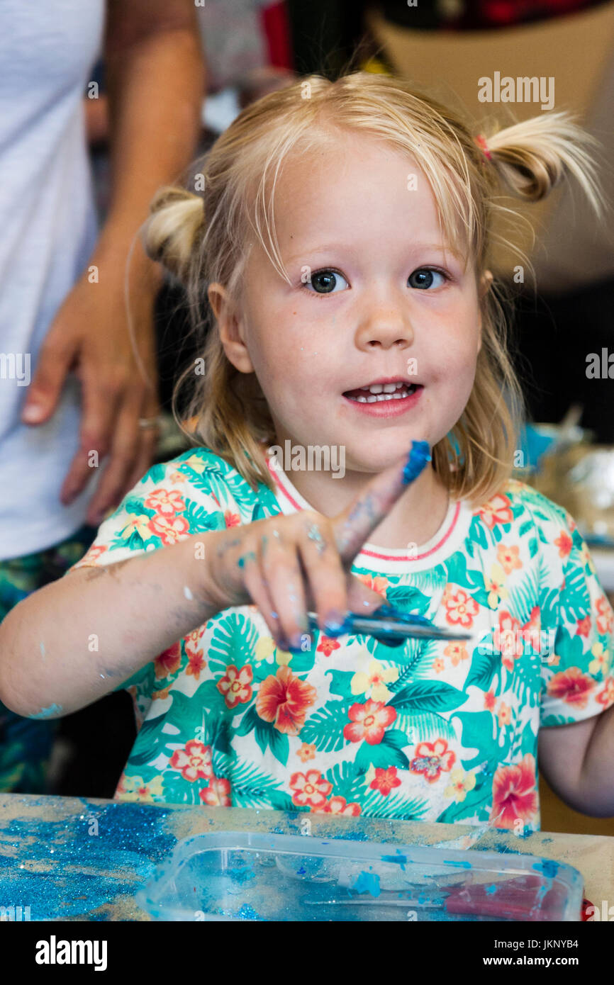 Kaukasische blonde Kind, Mädchen, 5-6 Jahre alt, Ihren Finger Anzeige mit blauer Farbe auf. Blick auf Viewer. Hallenbad in Kunst und Handwerk Lernwerkstatt. Stockfoto