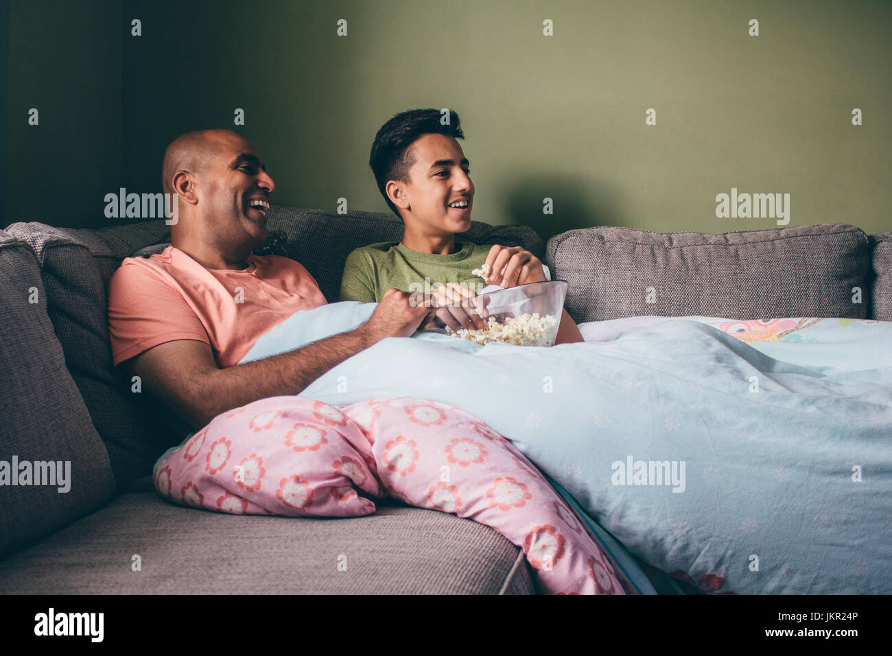 Vater und Sohn gemeinsam einen Film anschauen. Sie sind zusammengerollt auf dem Sofa mit Popcorn und lachst. Stockfoto