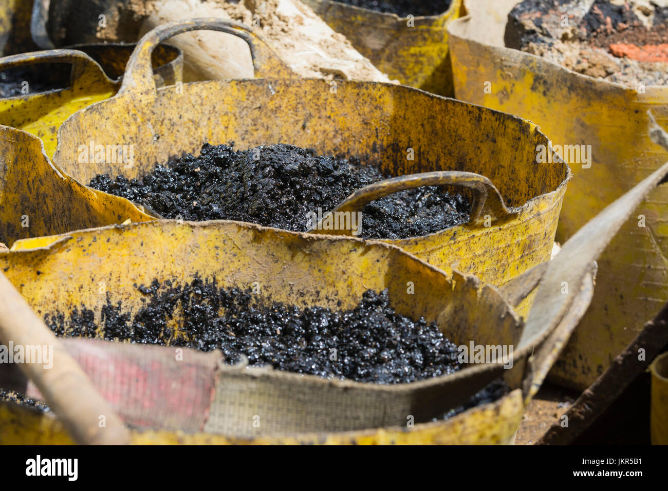 Bitumen in Eimern auf einer Baustelle in Straße Oberflächenersatz einsatzbereit. AKA Asphalt und Teer. Stockfoto