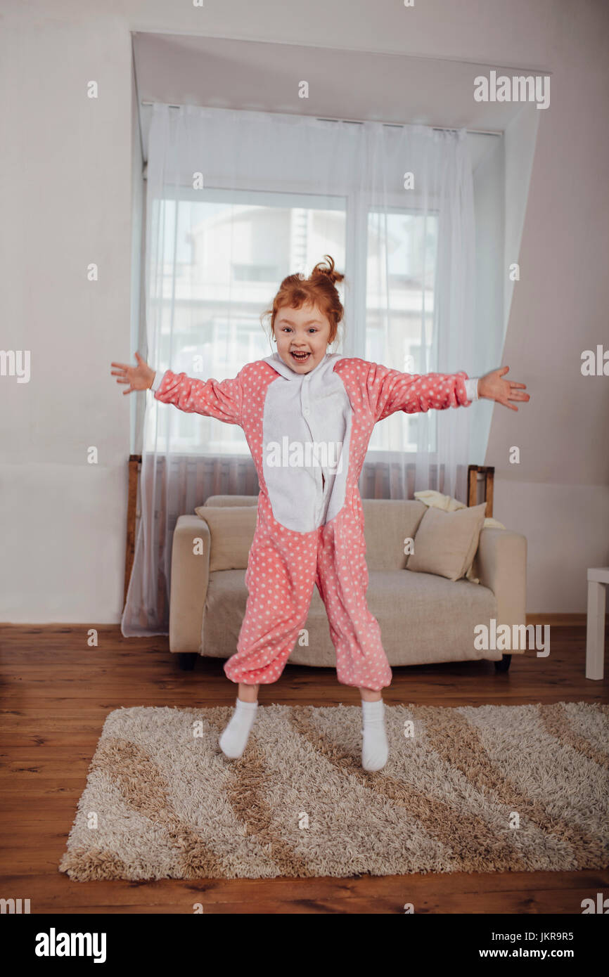 Fröhliches Mädchen mit ausgestreckten Armen springen über Teppich im Wohnzimmer zu Hause Stockfoto