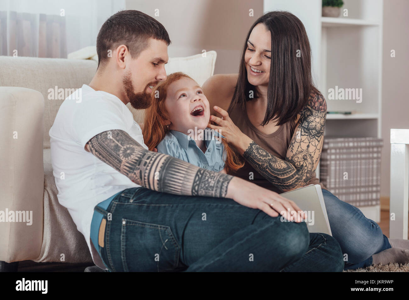Fröhliche Eltern spielen mit Tochter beim Sitzen auf dem Sofa im Wohnzimmer zu Hause Stockfoto