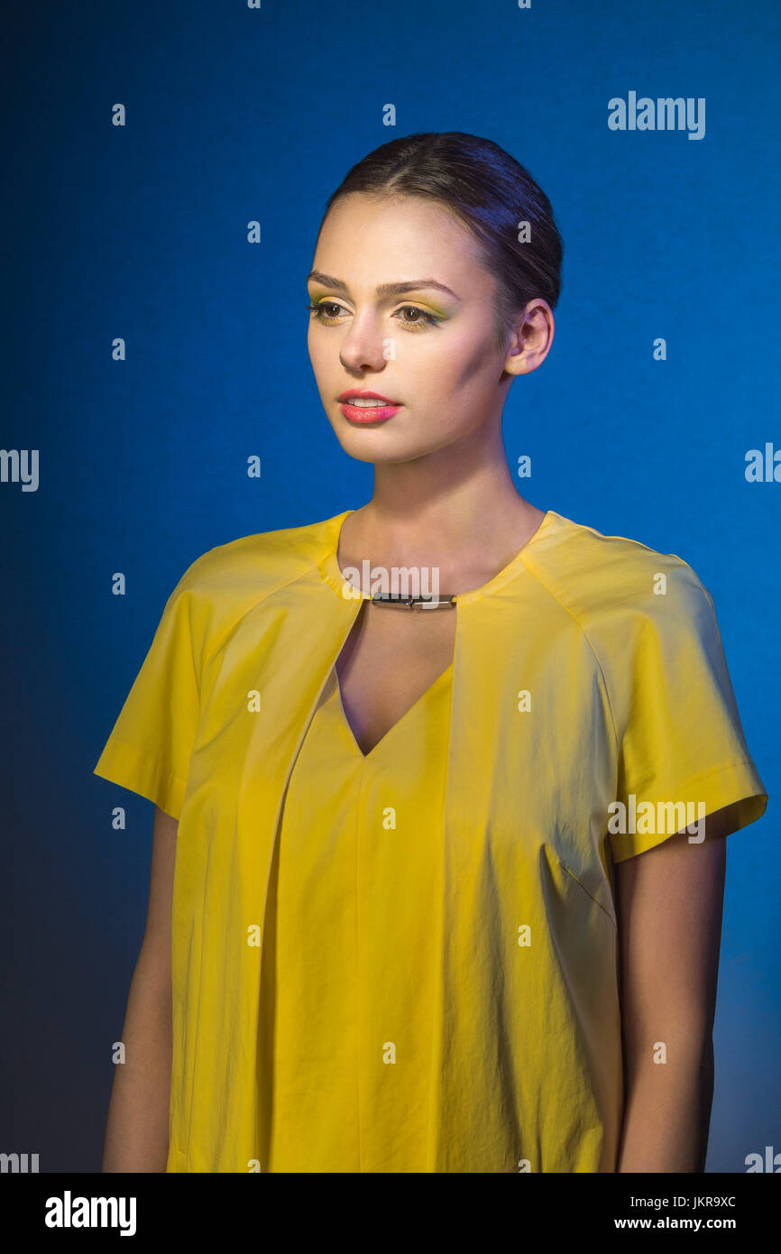 Lächelnde junge Mode Modell Wegsehen stehend vor blauem Hintergrund Stockfoto