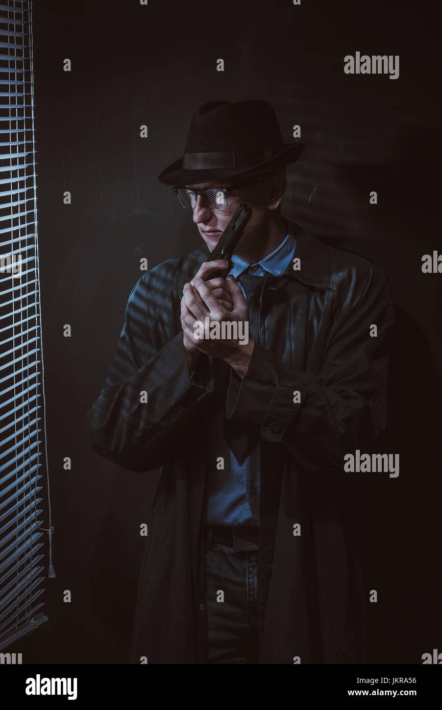 Junger Mann mit Gewehr durch Fenster gegen schwarze Wand Stockfoto