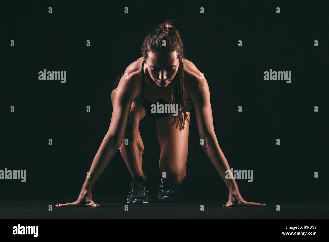Fokussierte Frau in Startposition auf schwarzem Hintergrund Stockfoto