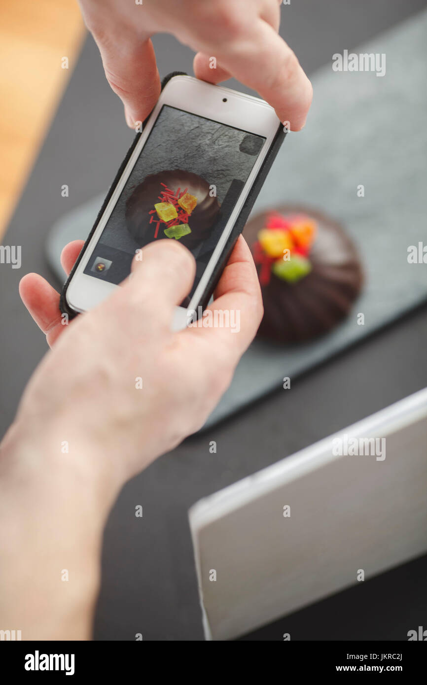 Bild des Menschen fotografieren Dessert am Tisch durch Handy zugeschnitten Stockfoto