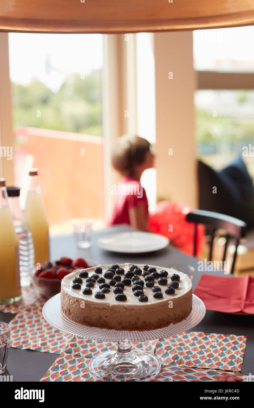 Kuchen am Stand über Tischsets am Esstisch mit Mädchen spielen im Hintergrund Stockfoto