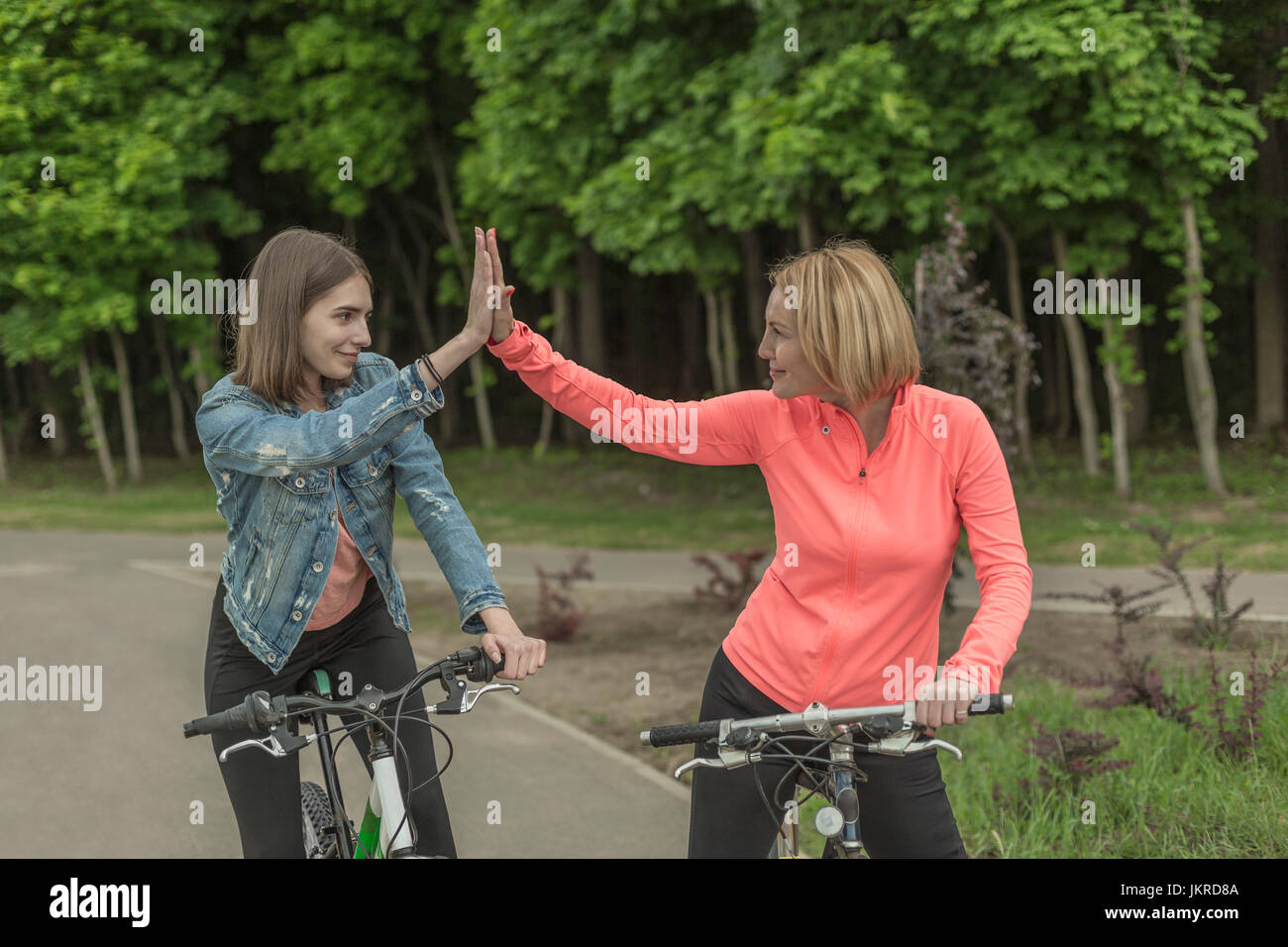 Lächelnde Mutter und Tochter tut High-Five beim Reiten Fahrrad im park Stockfoto