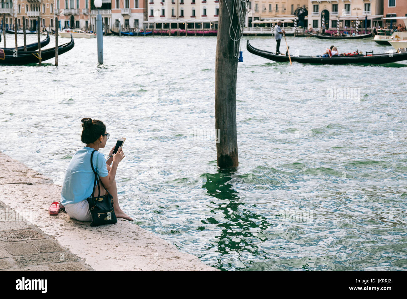 Junge Frau sitzt am Ufer des Canal Grande Handy surfen. Der Kanal ist die große Wasser-Verkehrskorridors in der Stadt. Stockfoto