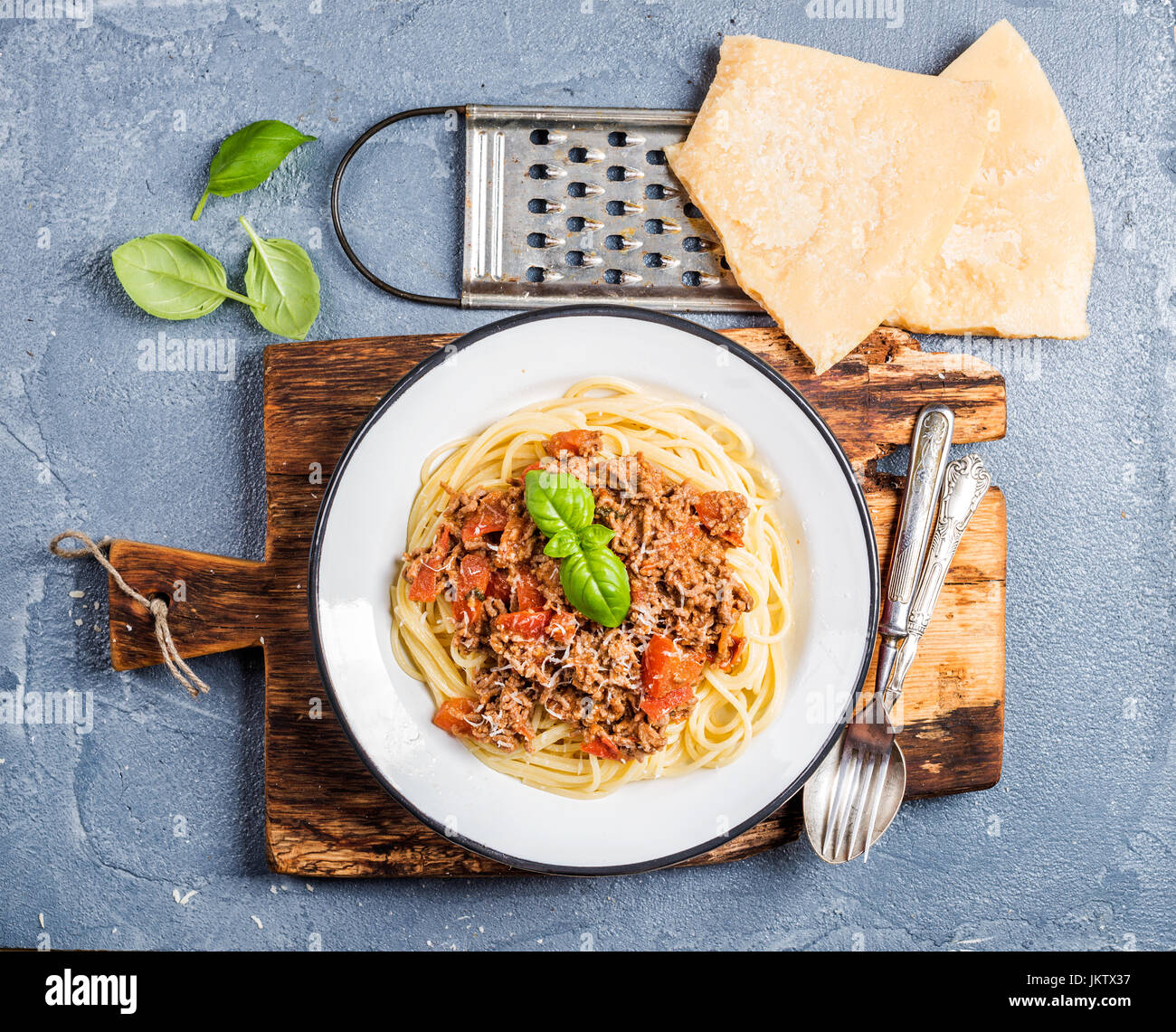 Pasta-Essen. Spaghetti Bolognese in Metallplatte auf rustikalem Holzbrett mit Parmesan-Käse, Reibe und frischem Basilikum über grauen Beton Hintergrund Stockfoto