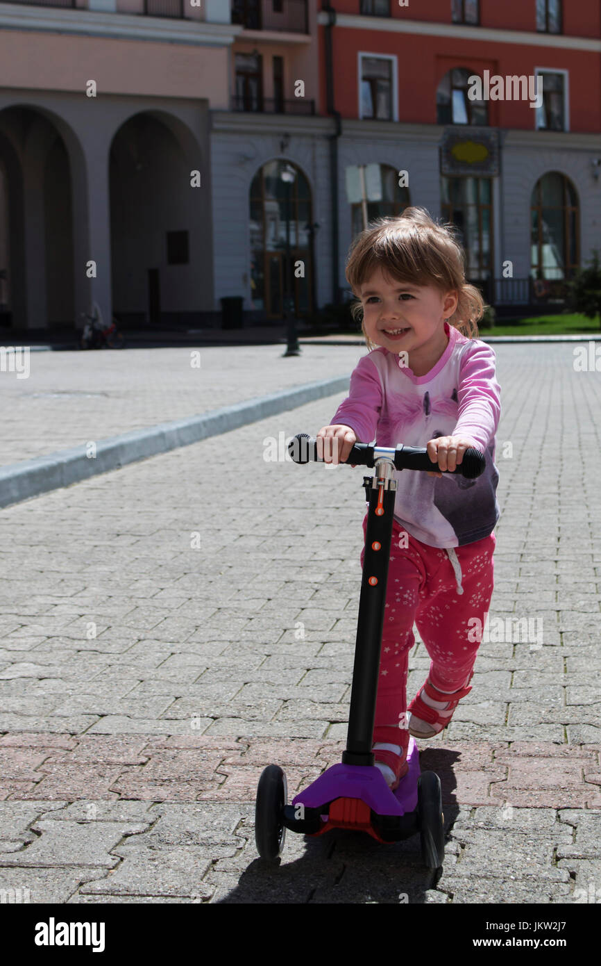 Lächelnd positive Mädchen reiten auf Roller in Stadt Stockfoto