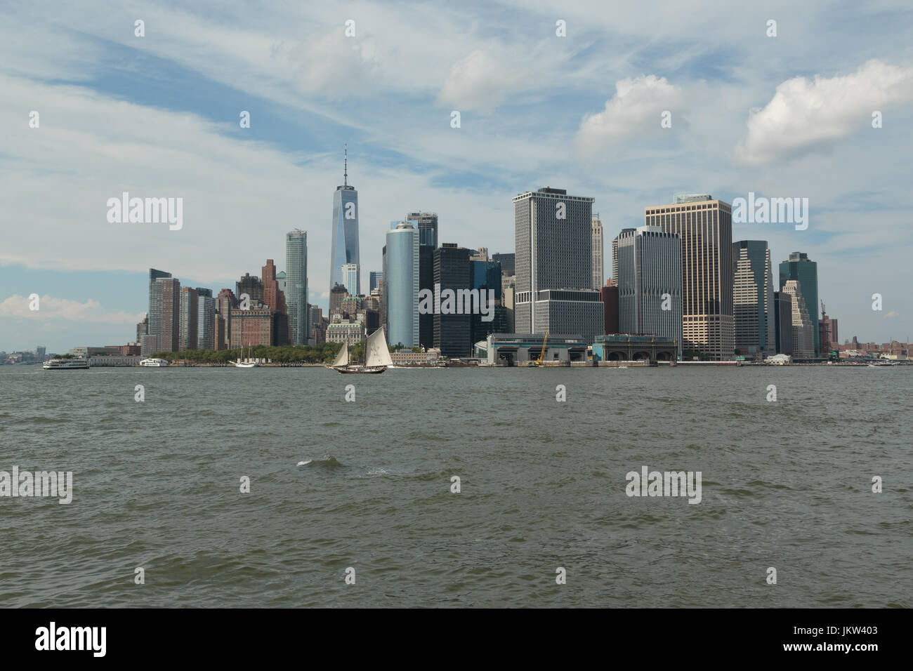 Ein Foto von der Skyline von Manhattan, wie von Governors Island, New York City zu sehen. Im Vordergrund ist ein altes Segelschiff zu sehen. Stockfoto