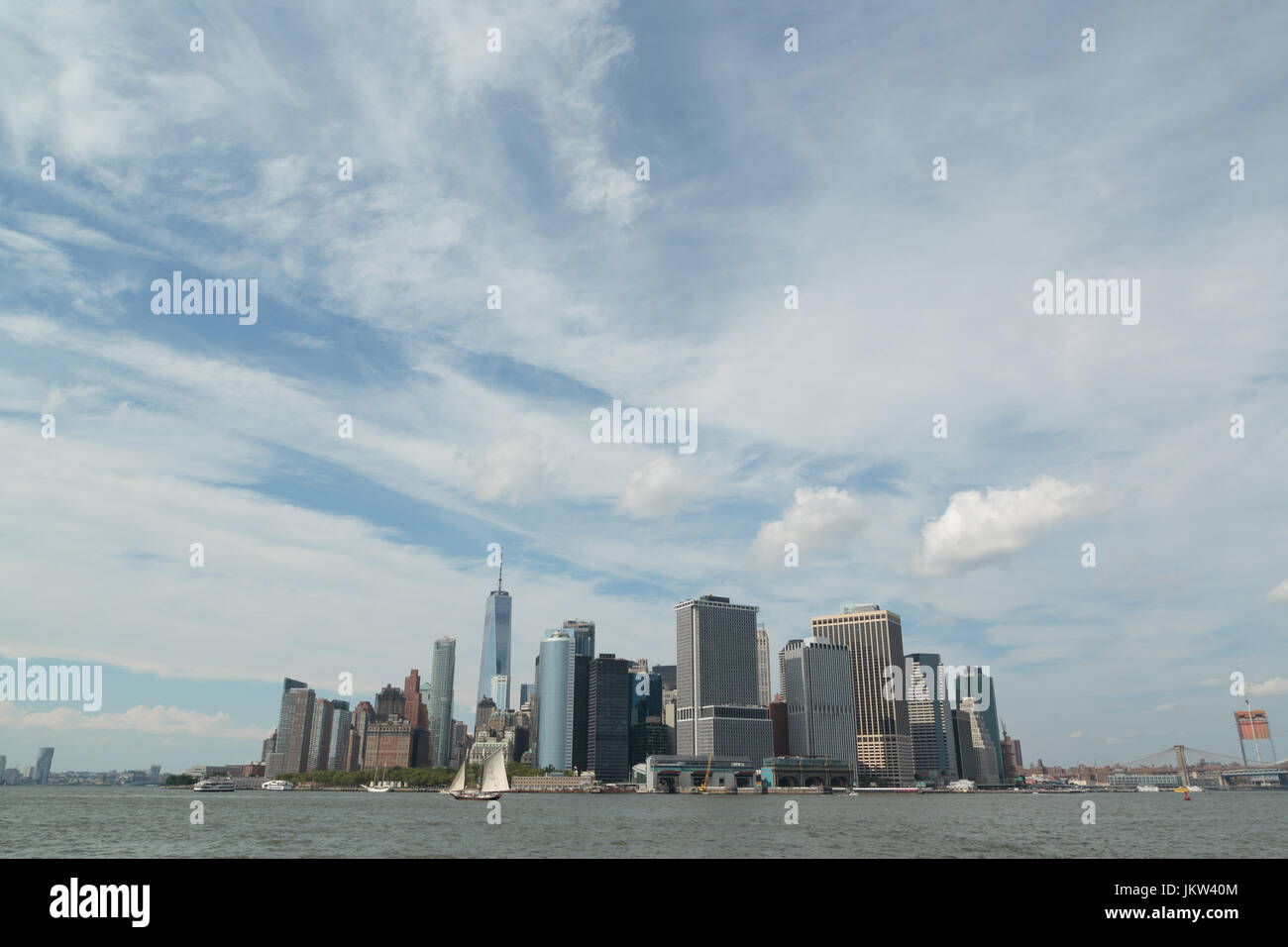 Ein Foto von der Skyline von Manhattan, wie von Governors Island, New York City zu sehen. Im Vordergrund ist ein altes Segelschiff zu sehen. Stockfoto