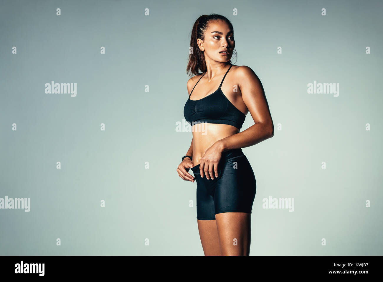 Porträt von Fitness-Frau von Sportswear über grauen Hintergrund stehen und wegsehen. Hispanische weibliches Model im Studio. Stockfoto