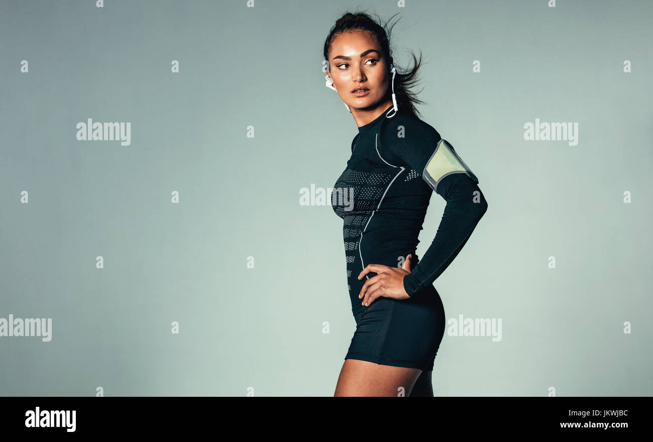 Porträt von Fit junge Frau, die Musik über Kopfhörer hören. Gesunde, muskulöse Frau mit Arm-Band auf grauem Hintergrund. Stockfoto