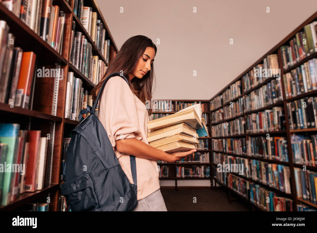Junge Studentin tragen viele Bücher in der Universitätsbibliothek. Kaukasische Schüler lesen Bücher in der Bibliothek. Stockfoto