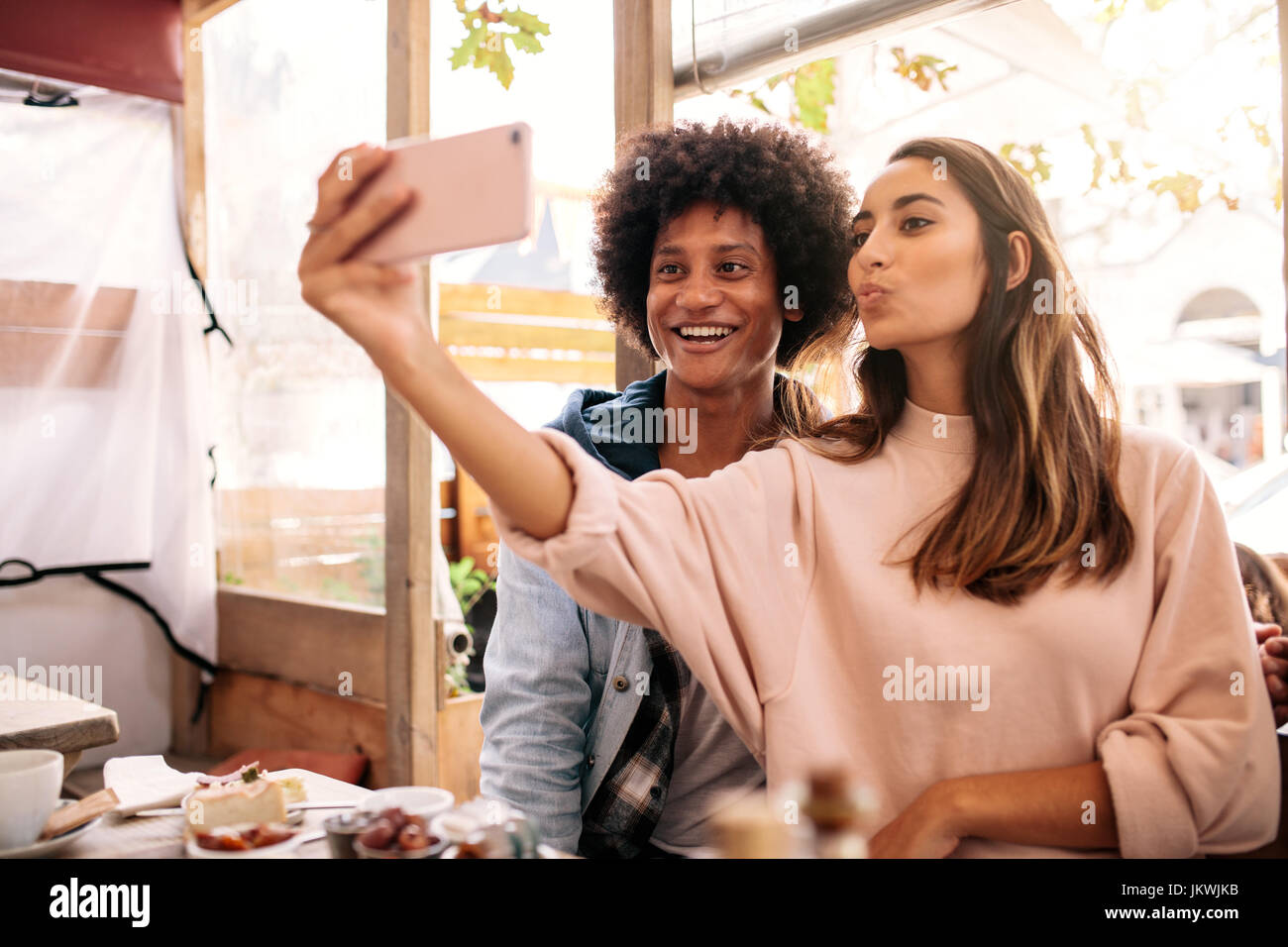 Junge Frau nehmen Selfie mit afrikanischen Mann in der Cafeteria. Junges Paar Smartphone im Café betrachten. Stockfoto