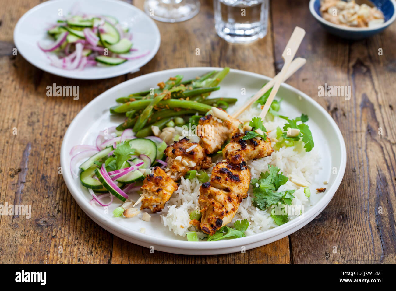 Satay-Hähnchen-Spieße mit grünen Bohnen, Reis und Gurkensalat Stockfoto