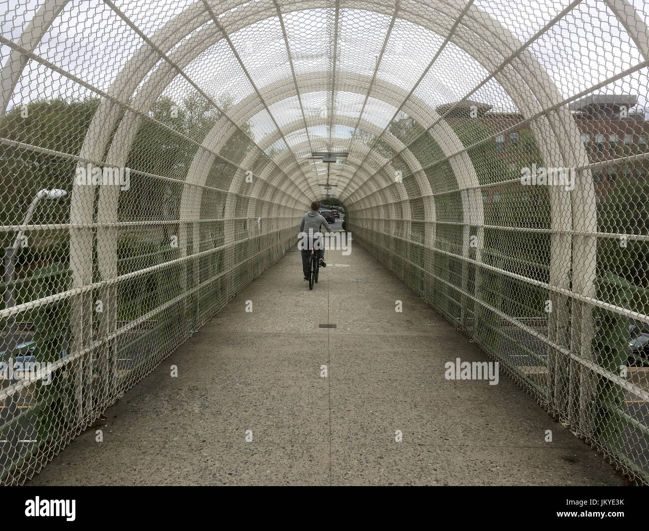 Frau in schwarz fährt Fahrrad auf einer Überführung über die Autobahn in Brooklyn New York an einem grauen Nachmittag. Transport-Alternativen, Fortbewegung t Stockfoto