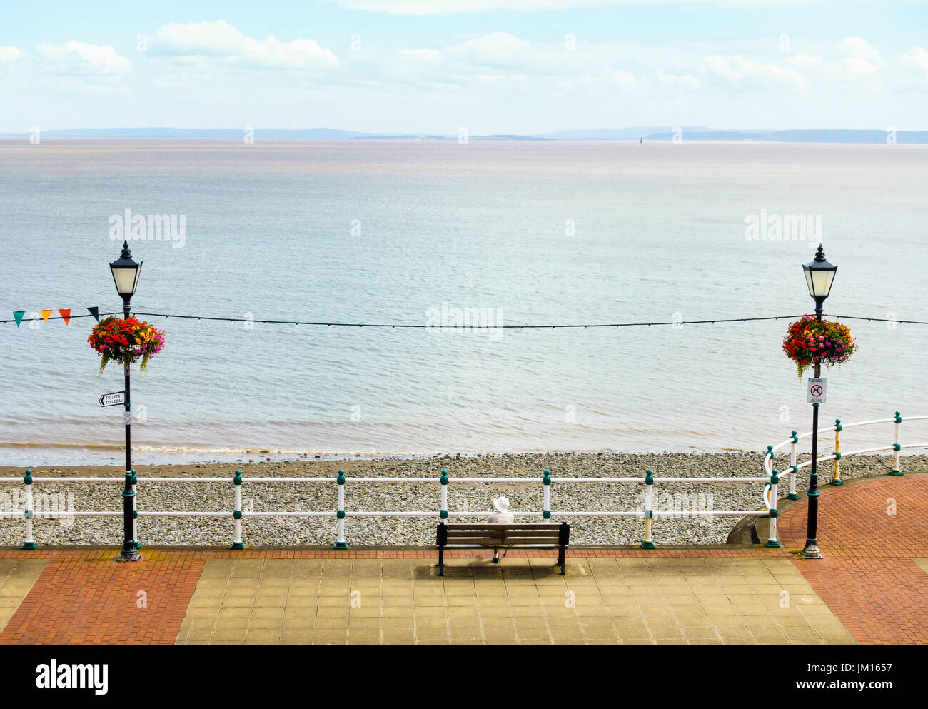 Luftaufnahme von einer älteren Frau sitzen auf einer Bank an der Esplanade in Penarth, Blick auf das Meer. Stockfoto