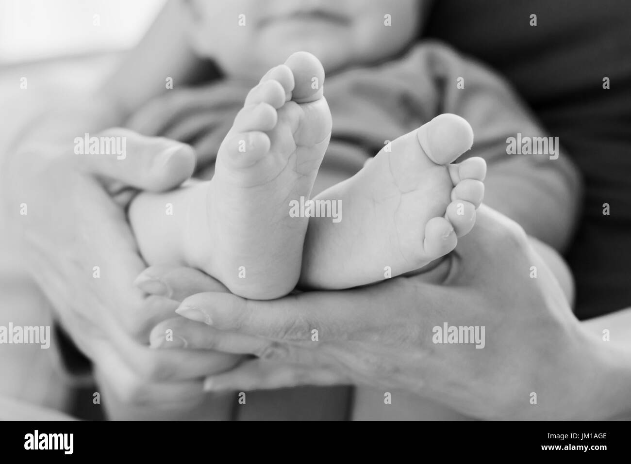 Nahaufnahme der Füße des Kindes in Mutters Händen. Foto gemacht in schwarz / weiß Stockfoto