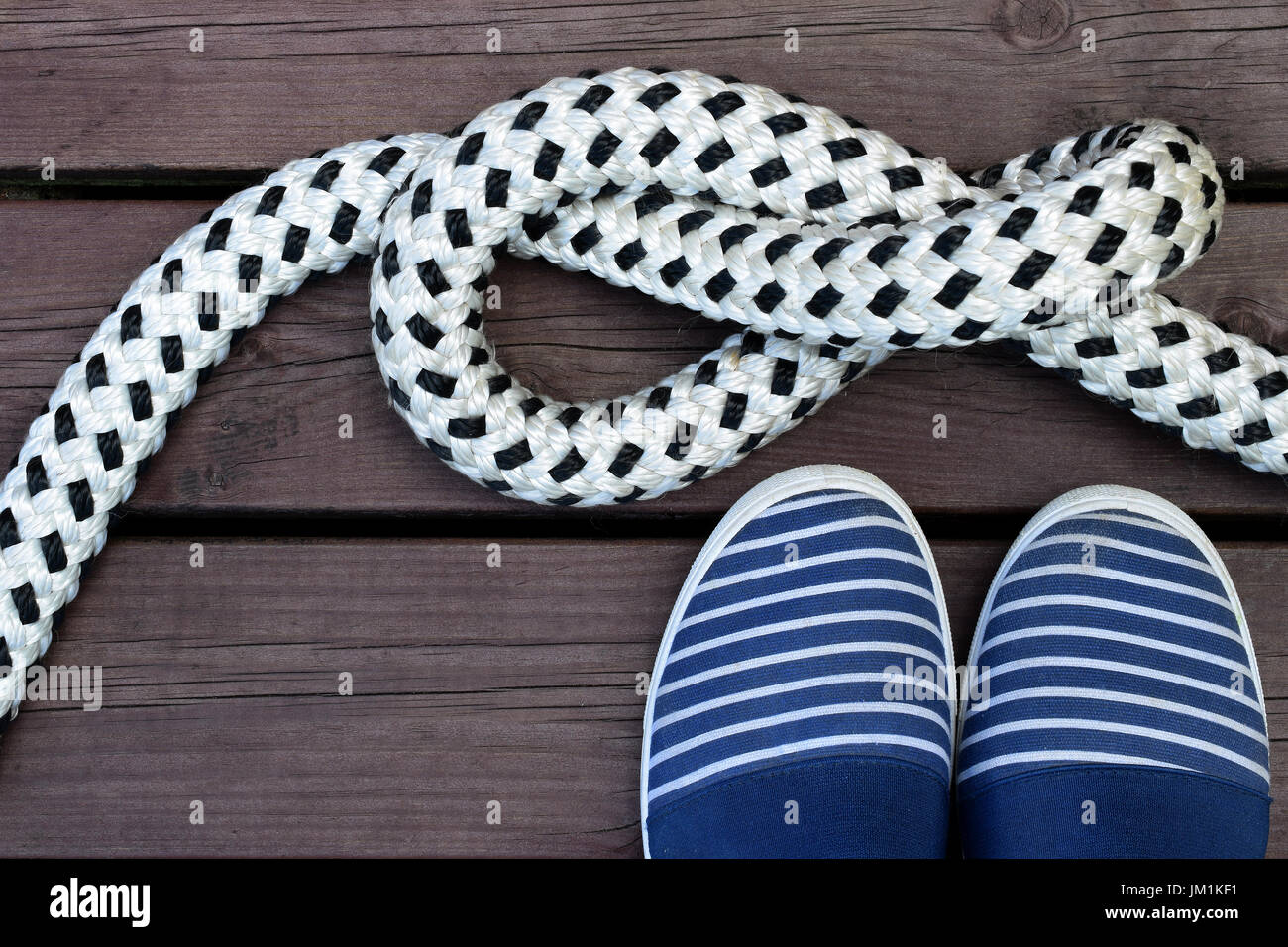 Blau-weiß gestreiften Seemann Stil Schuhe und Seil mit einem Knoten auf einen braunen Holz dock Stockfoto