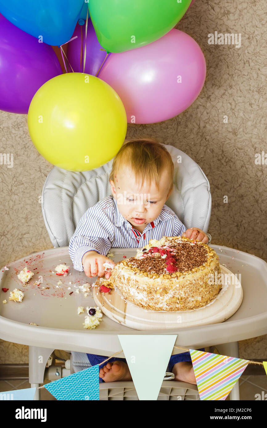 Ein Jahr alter Junge sitzt im Hochstuhl und seinen Kuchen schmecken. Ersten Geburtstag feiern Konzept. Kuchen-smash Stockfoto