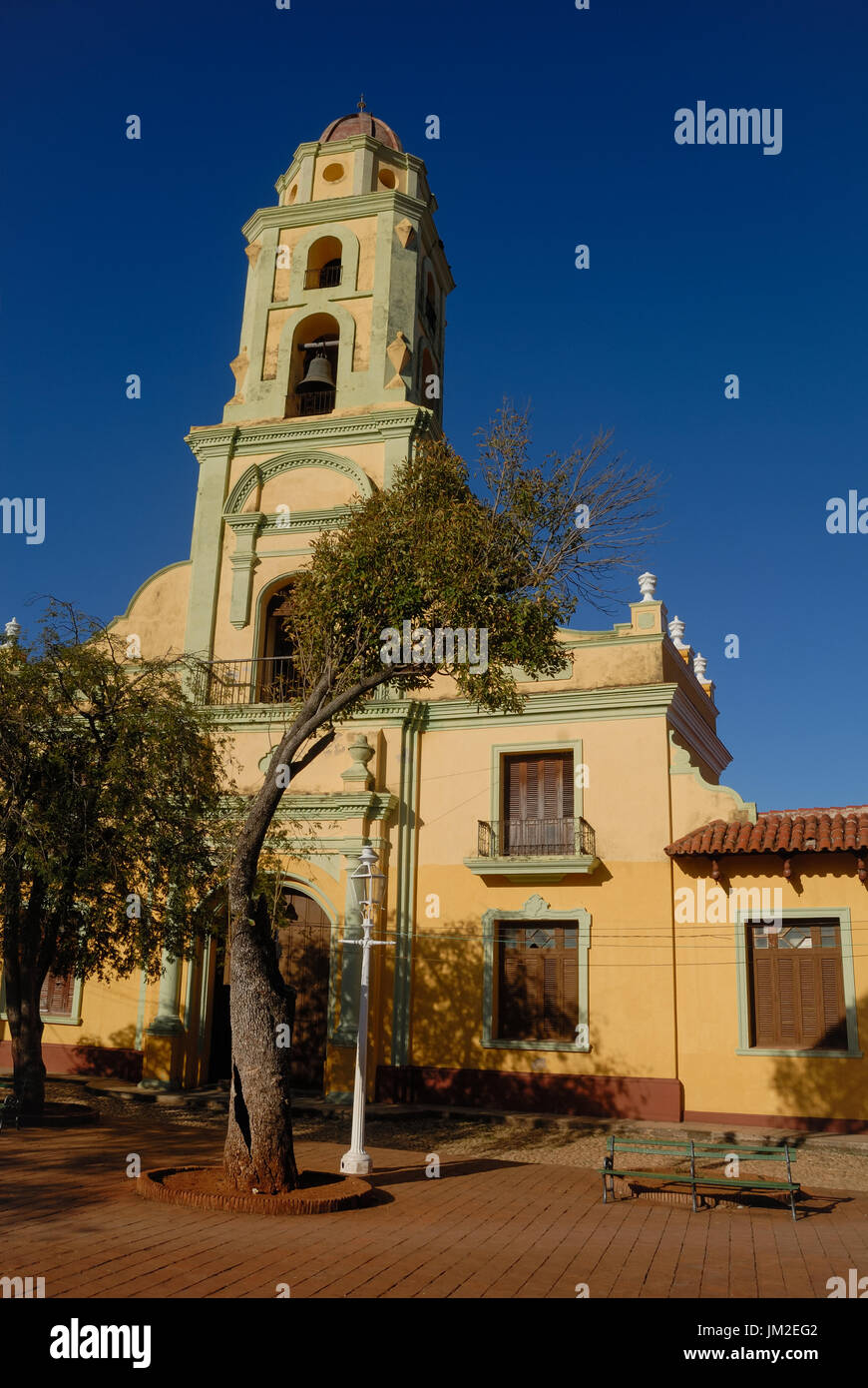 Der Kirchturm von dem Platz in Trinidad, Kuba mit Bank und Baum vor der Kirche. Stockfoto