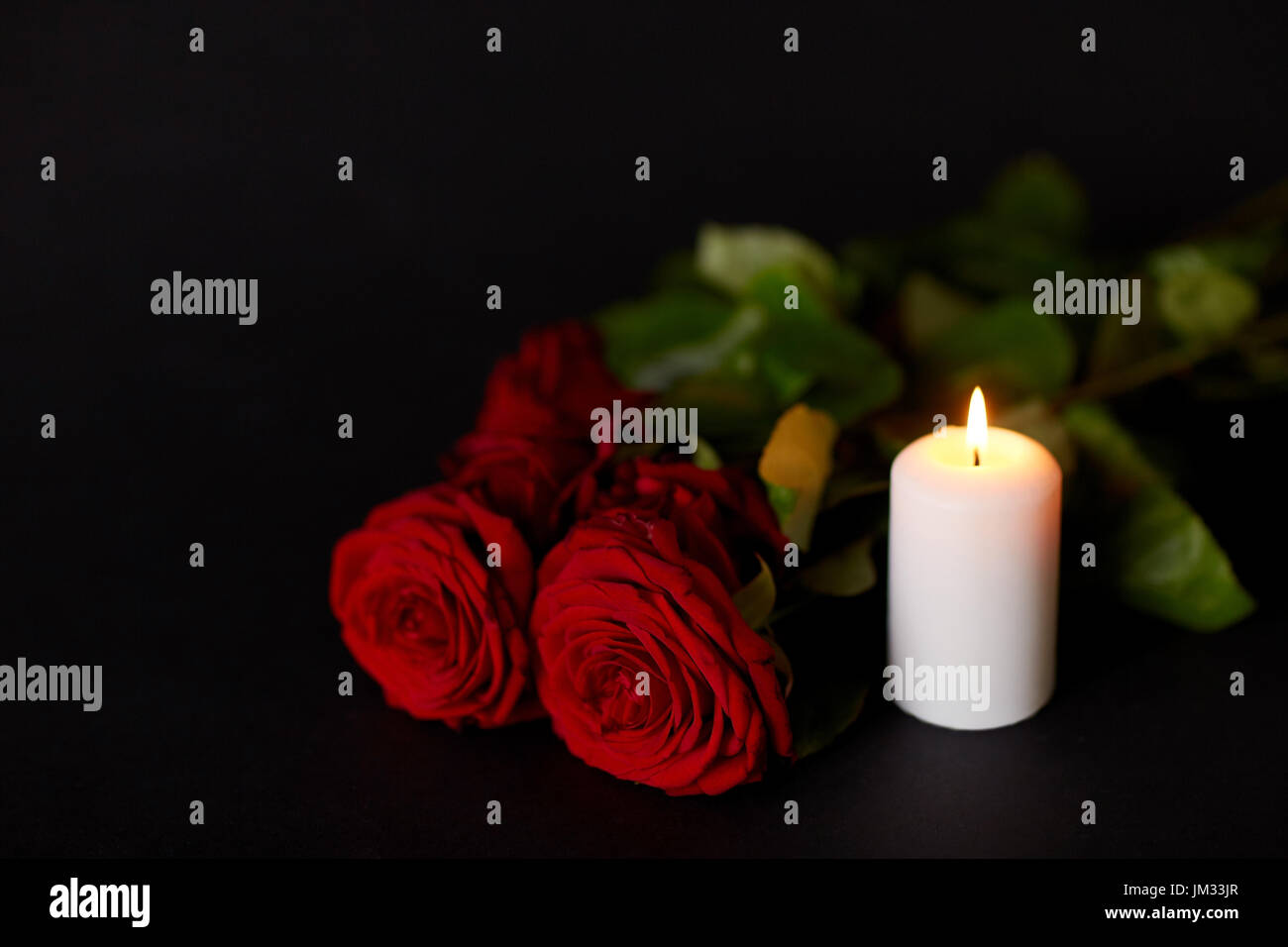 rote Rosen und brennende Kerze über schwarzen Hintergrund Stockfoto